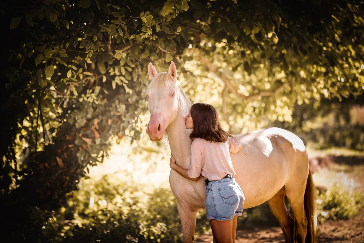 Elia Grimaud embracing a horse beneath a sun-dappled tree